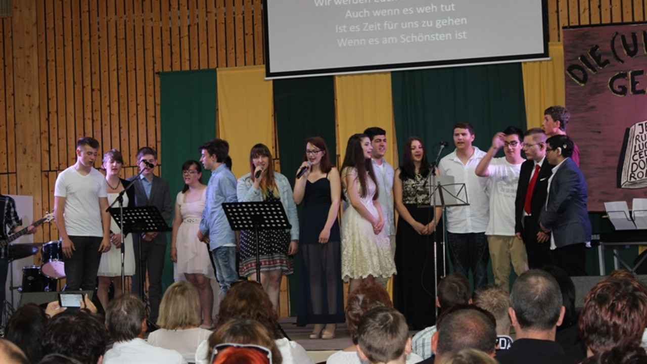 Schüler singen ein Abschlusslied auf der Bühne. 