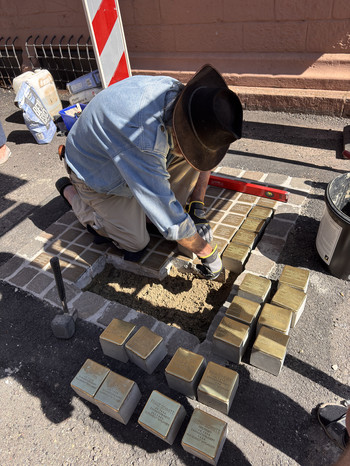 Mann kniet auf dem Boden und verlegt die Stolpersteine.