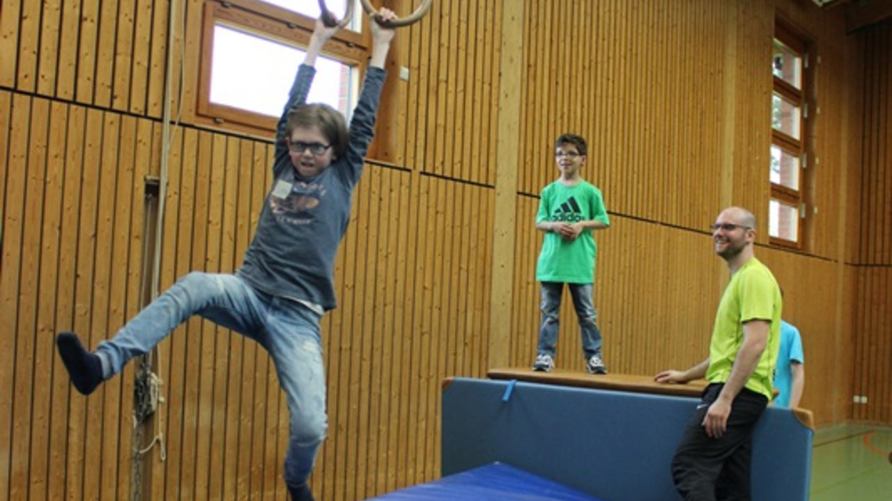 Kind schwingt an Ringen in der Turnhalle.