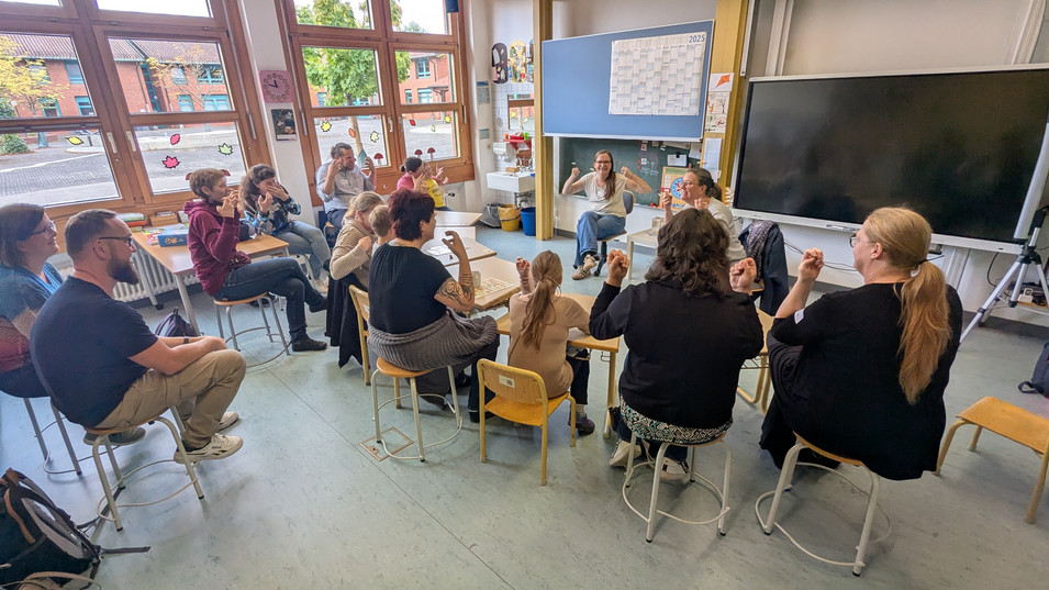 Im Klassenzimmer üben Teilnehmer*innen Gebärden mit 2 BU-Fachkräften.