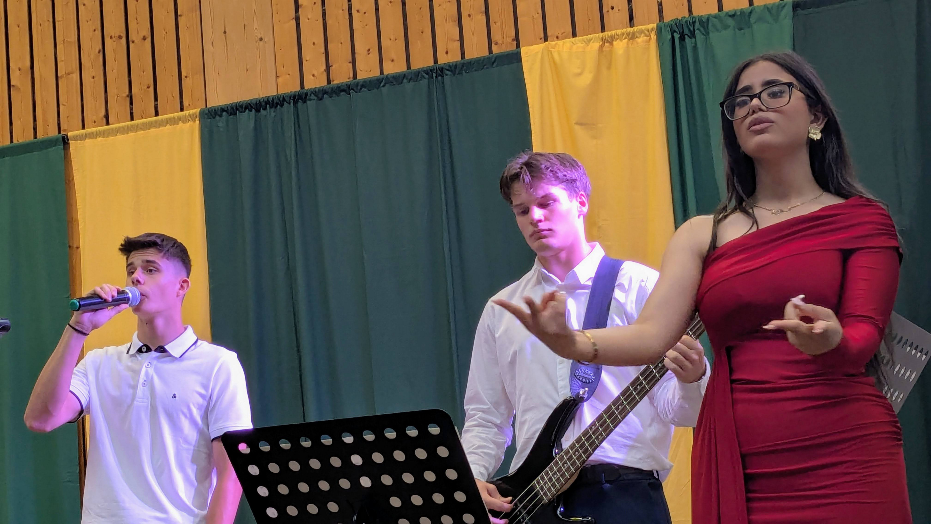Eine Schülerin und ein Schüler singen und ein Schüler spielt Gitarre auf der Bühne 