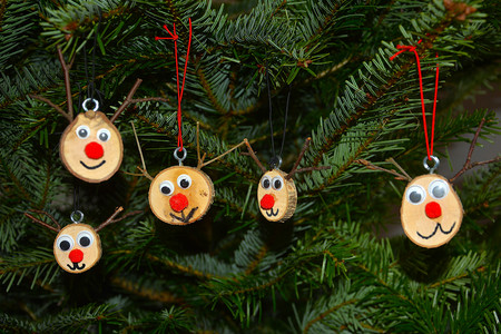 Gebastelte kleine Baumscheiben mit Augen, Nase und Mund und 2 Ästchen als Rentier als Baumschmuck am Tannenbaum 