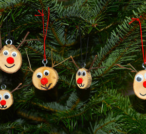 Gebastelte kleine Baumscheiben mit Augen, Nase und Mund und 2 Ästchen als Rentier als Baumschmuck am Tannenbaum 