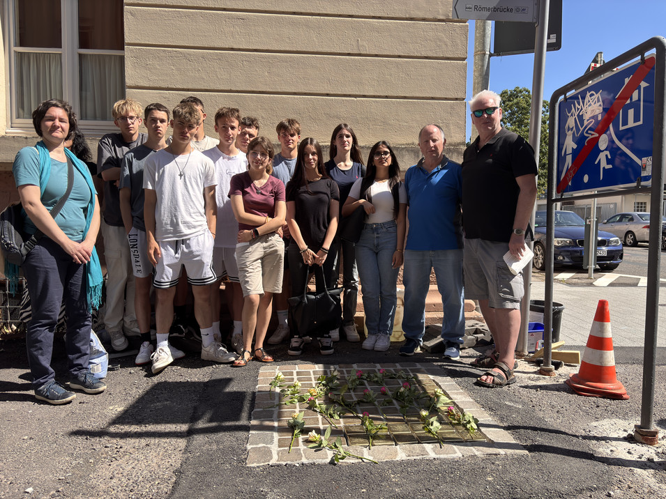 Gruppenfoto mit allen Akteuren vor den rosengeschmückten Stolpersteinen