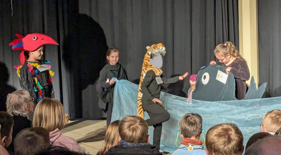 Schüler als Papagei, als Löwe verkleidet. Schüler halten ein blaues Tuch als Zeichen des Wassers. 