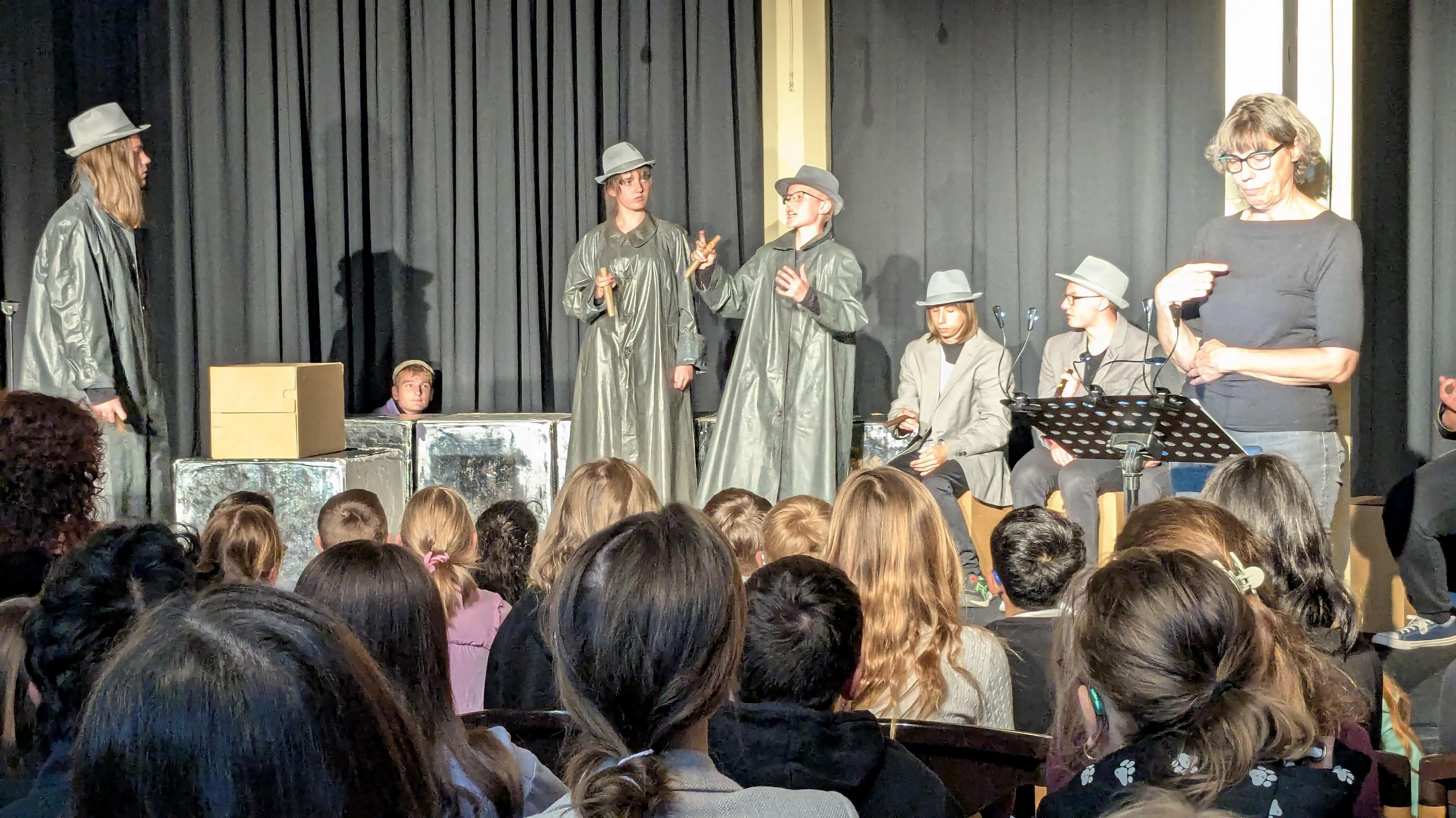 Schüler sind verkleidet als graue Herren mit langen dunklen Mänteln. 