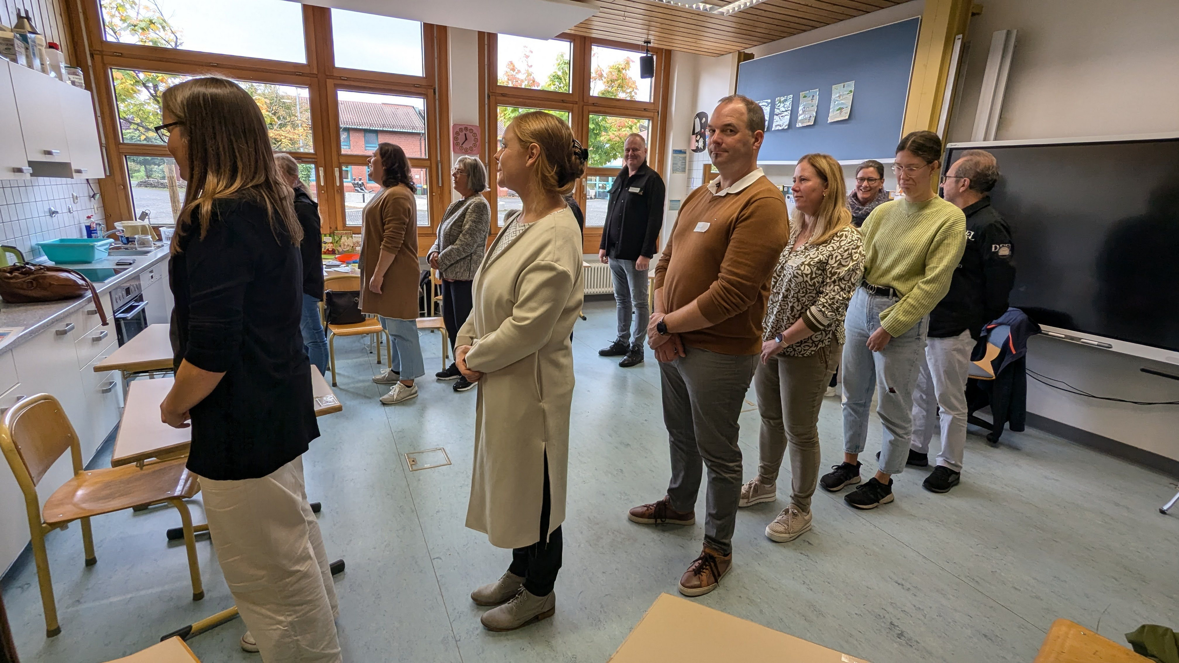 Im Rahmen eines Gebärdensprachkurses stehen Erwachsene in 2 Reihen im Klassenraum. 