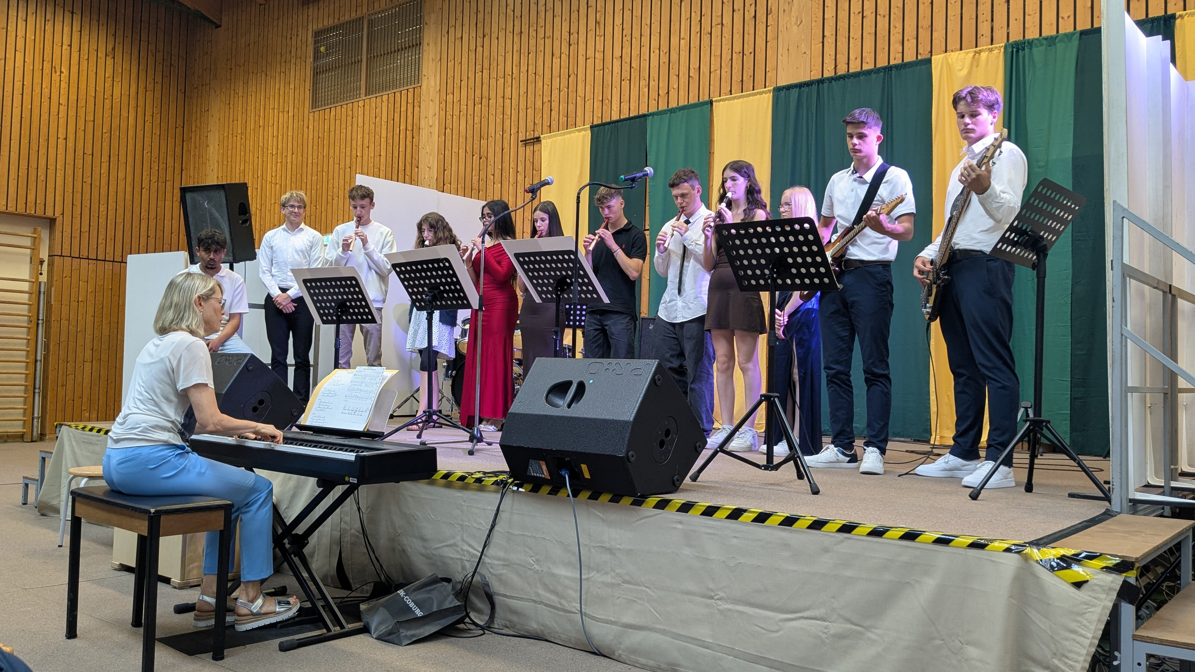 Die Entlassschülerinnen und Schüler teilweise mit Instrumenten auf Bühne in der Turnhalle 
