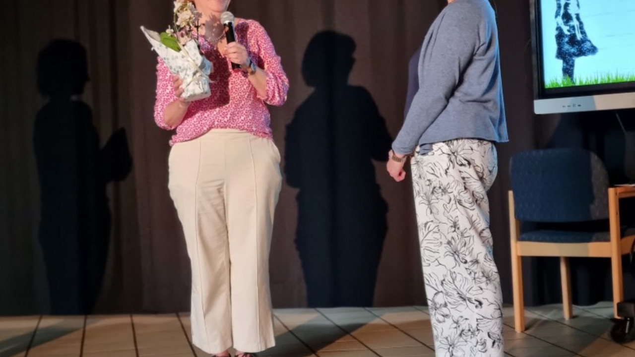 Frau Moog überreicht Frau Ostermann einen Blumenstock. 