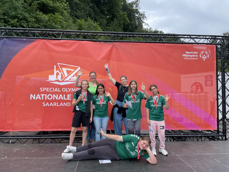 4 Schülerinnen und 1 Schüler mit umgehängten Urkunden mit Lehrkräften vor dem Banner Special Olympics