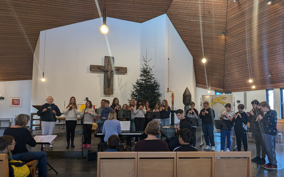 Schülerinnen und Schüler spielen Flöten und gebärden in der Nähe des Altares in der Kirche