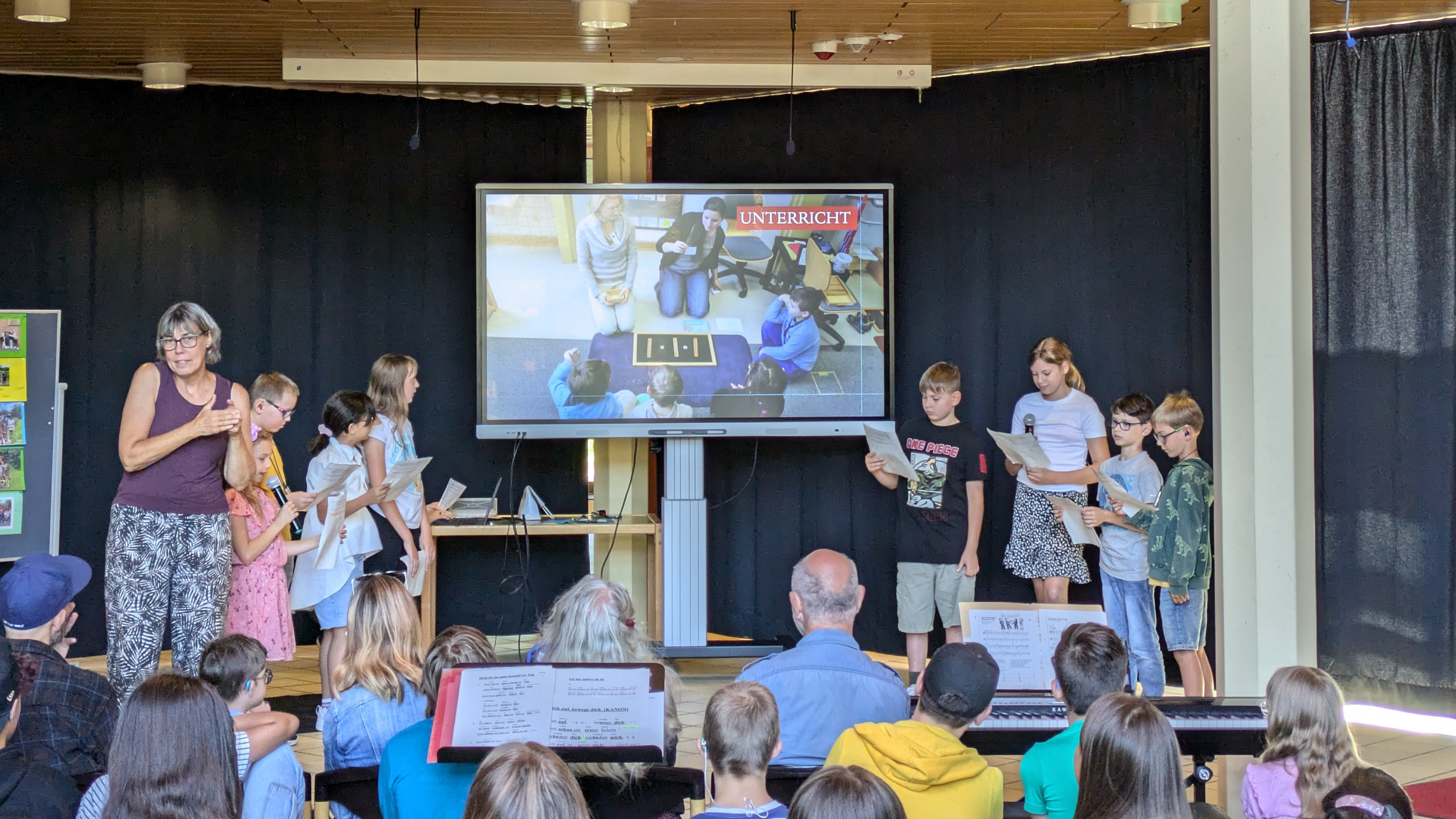 Mehrere Schülerinnen und Schüler stellen auf der Bühne die WHC mit Hilfe des Smartboards vor. 