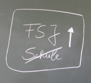 Schriftzug FSJ mit Pfeil nach oben und Schule durchgestrichen mit weißer Kreide auf grüner Tafel