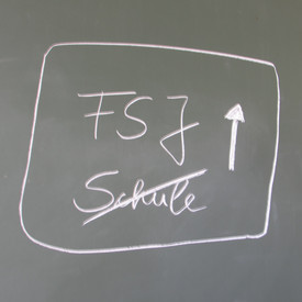 Schriftzug FSJ mit Pfeil nach oben und Schule durchgestrichen mit weißer Kreide auf grüner Tafel