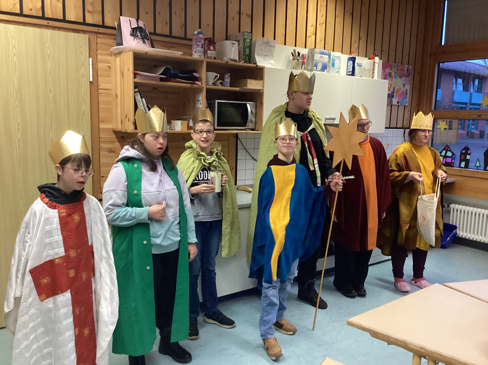 Sieben Sternsinger der Klasse GE 2 stehen in festlichen Kostümen bereit. Ein Schüler hält den Stern, der zur Krippe führt