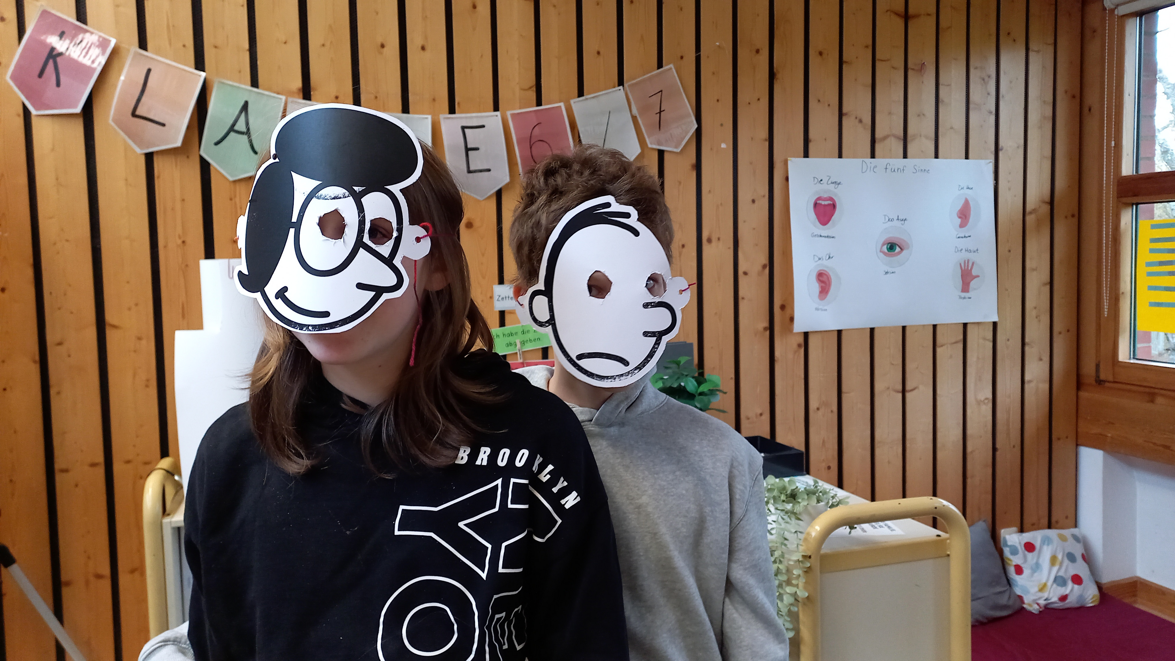 2 Schüler mit Papiermasken vor dem Gesicht 