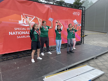 4 Schülerinnen und 1 Schüler stehend vor dem Banner Special Olympics halten die Urkunden in die Luft