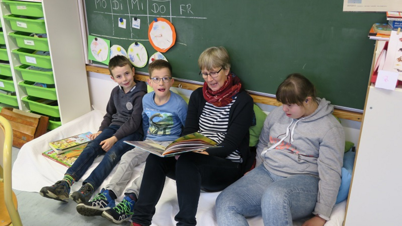 Lehrerin liest den Schülerinnen und Schüler ein Buch vor