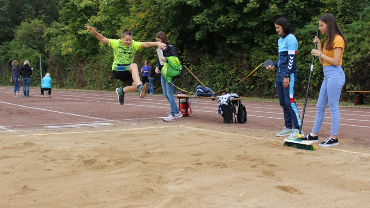 Schüler springt in einen Sandgraben 