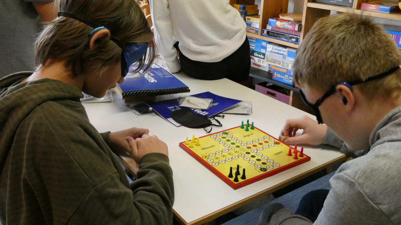 Schüler*innen spielen mit Augenmaske ein Brettspiel 