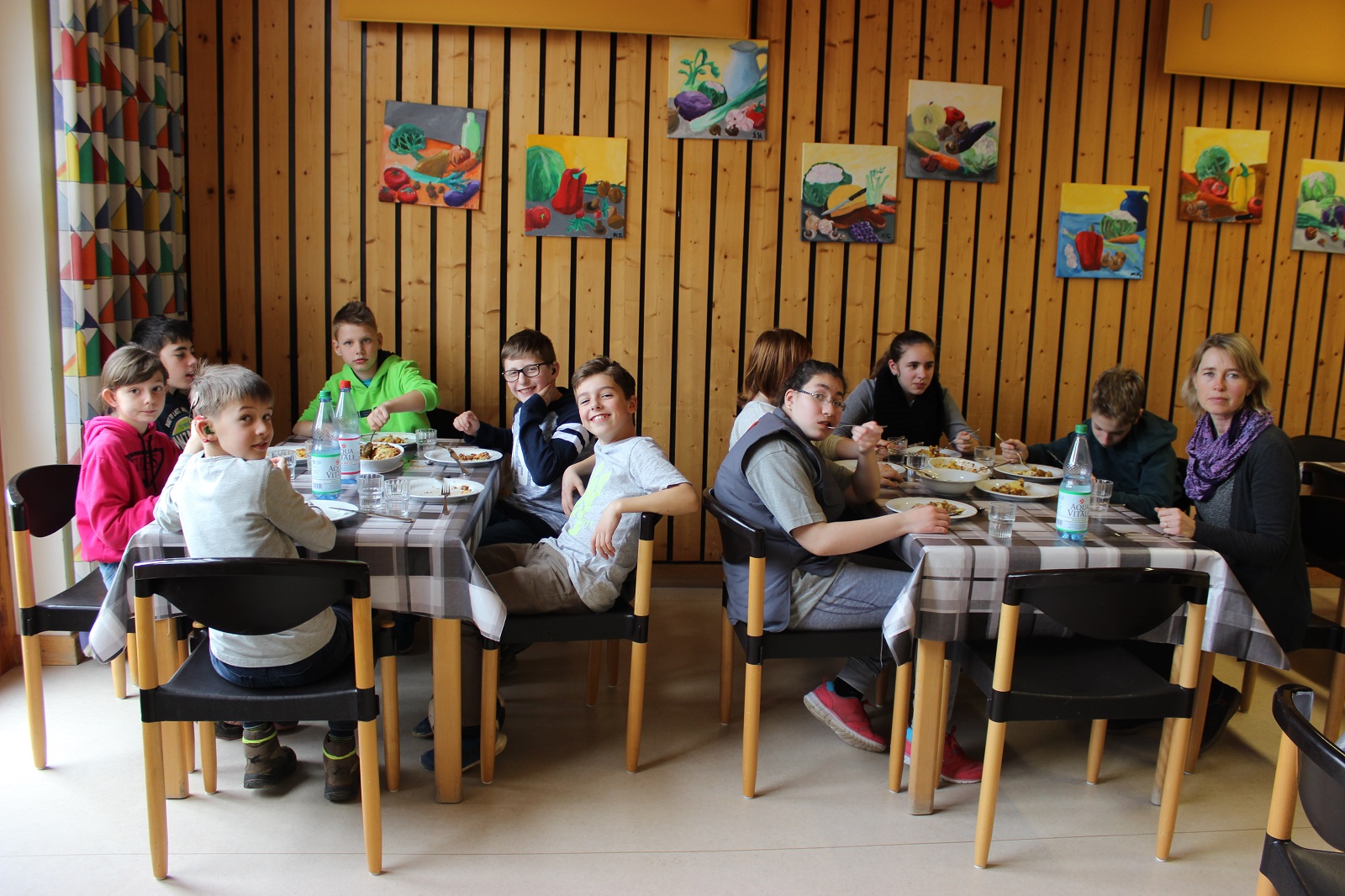 Kinder sitzen an Esstischen beim Mittagessen in der Mensa